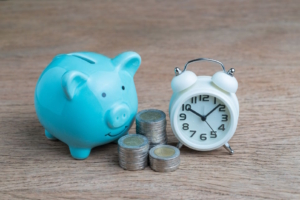 Cute blue piggy bank, a stack of coins, and a clock